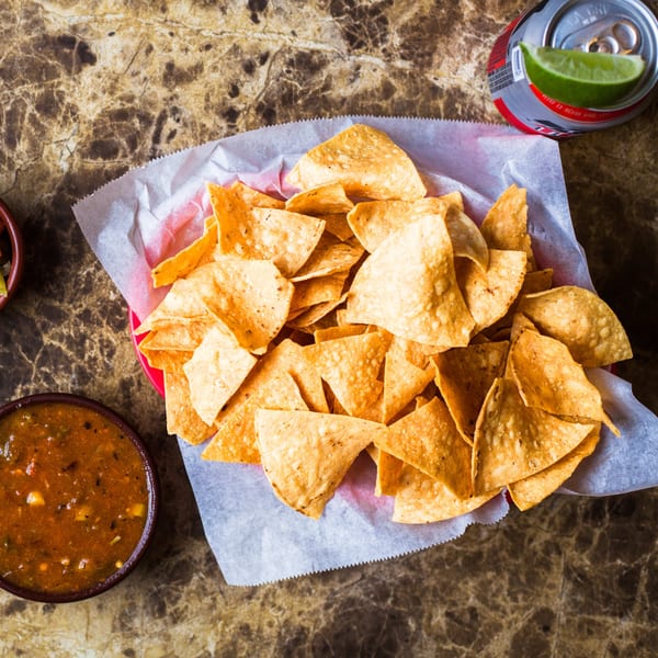 A basket of Gorditos tortilla chips with salsa and a soda with lime on a marble table.