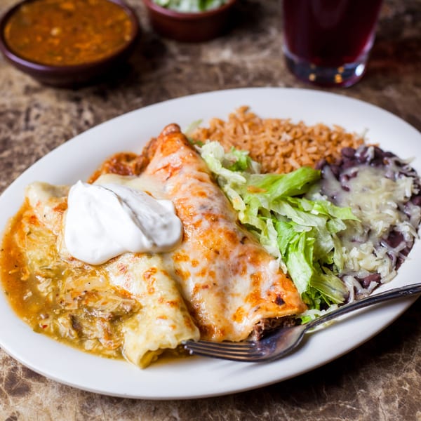 Gorditos' enchiladas with sour cream, rice, beans, and lettuce on a white plate.