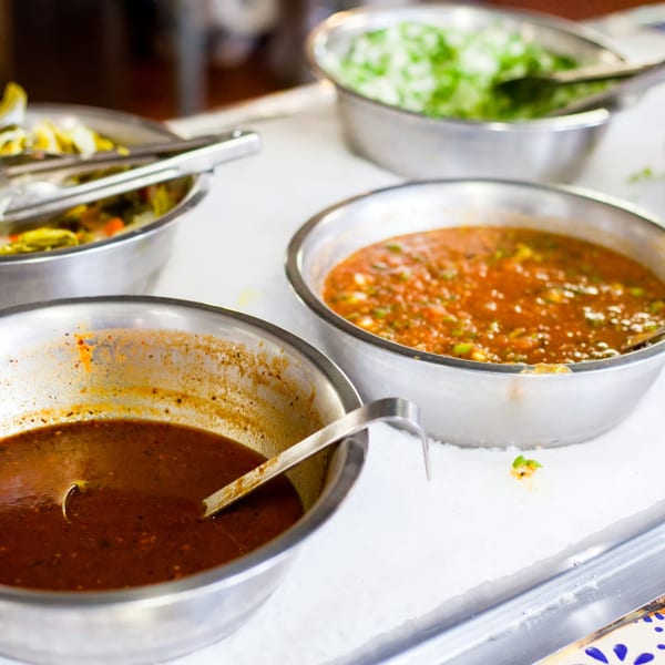 Stainless steel bowls of red and green salsas, and pickled vegetables on an ice bed.