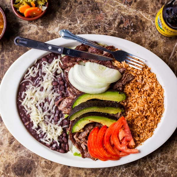 Gorditos' carne asada plate with rice, beans, avocado, tomatoes, and onions on a marble table.
