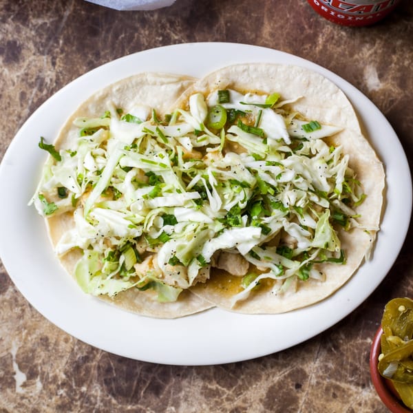 Two Gorditos tacos with shredded cabbage, green onions, and cilantro on a white plate.