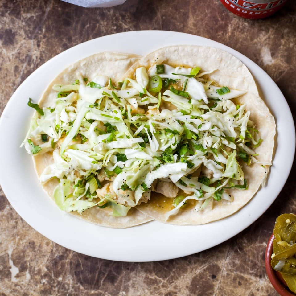 Two Gorditos tacos with shredded cabbage, green onions, and cilantro on a white plate.