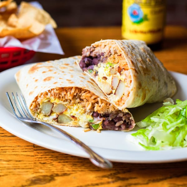 A Gorditos burrito, cut in half, revealing rice, beans, potatoes, and eggs, with a side of lettuce.