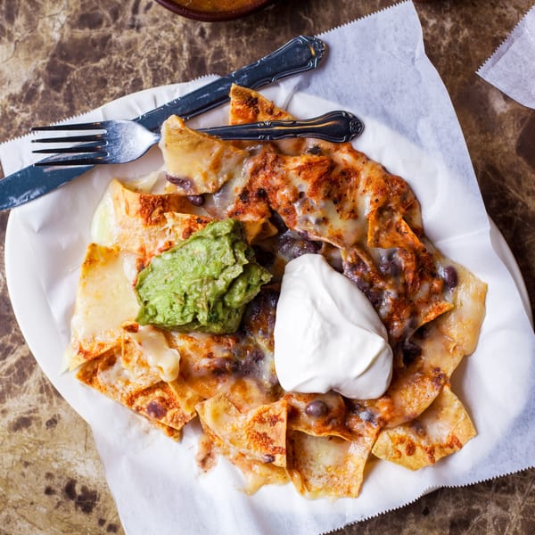 Gorditos' cheesy nachos with guacamole and sour cream on a white plate with silverware.