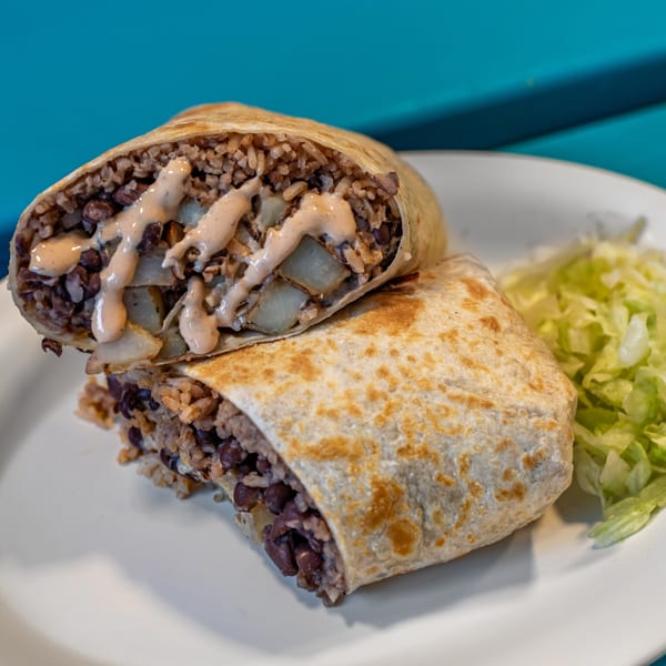 A Gorditos burrito, cut in half, filled with rice, beans, and potatoes, drizzled with sauce.